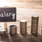Close-up Of Salary Text On Small Chalk Board With Increasing Coin Stack On Wooden Table